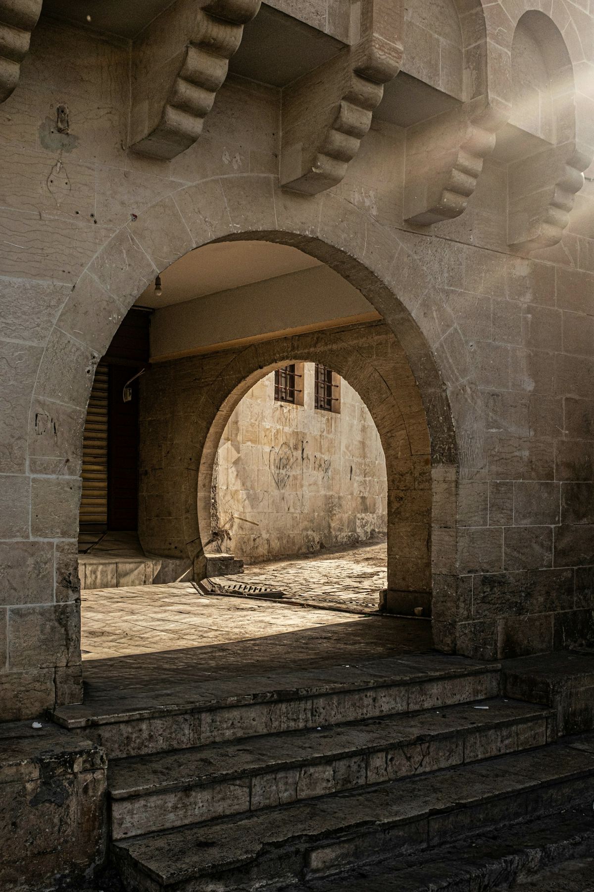 A stone arcade with worn steps, lit by sunlight falling through an archway.